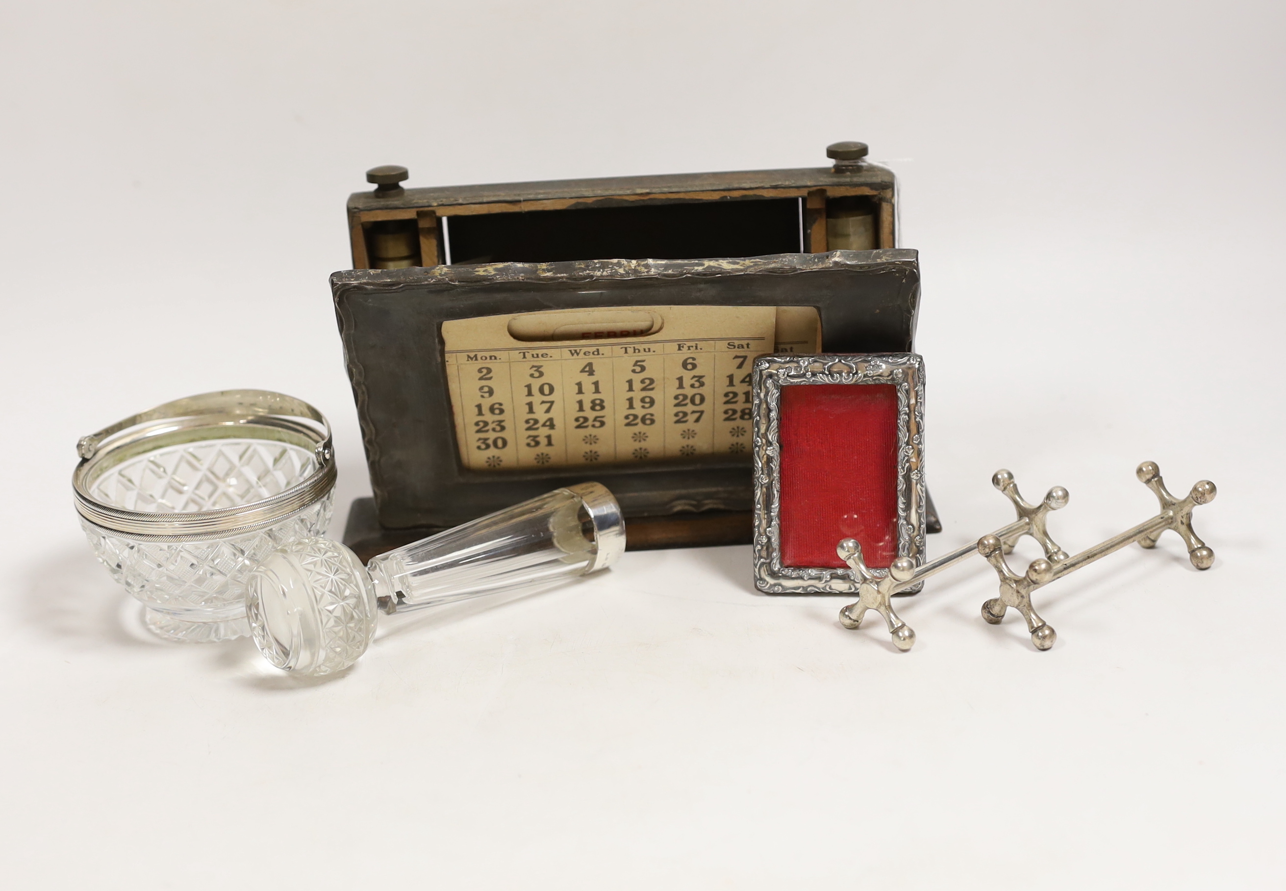 A pair of Edwardian silver knife rests, William Hutton & Sons, London, 1908, 77mm, a silver mounted wooden desk calendar, a late Victorian small silver mounted photograph frame, a silver mounted glass posy vase and a whi